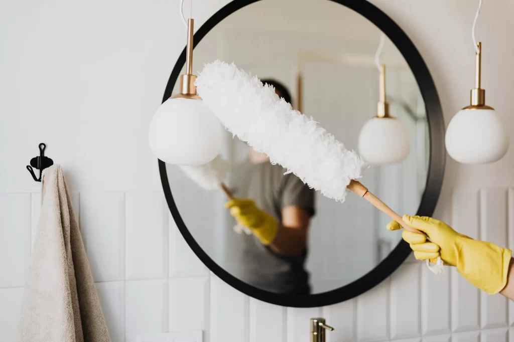 Person cleaning mirror with dusting brush