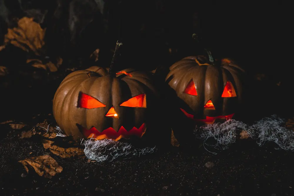 two pumpkins outside in the dark lit up from the inside